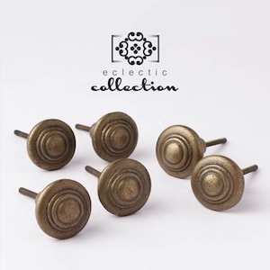 May include: Six antique bronze cabinet knobs with a circular, ridged design. The knobs are arranged on a white background. The text "eclectic collection" is above the knobs.