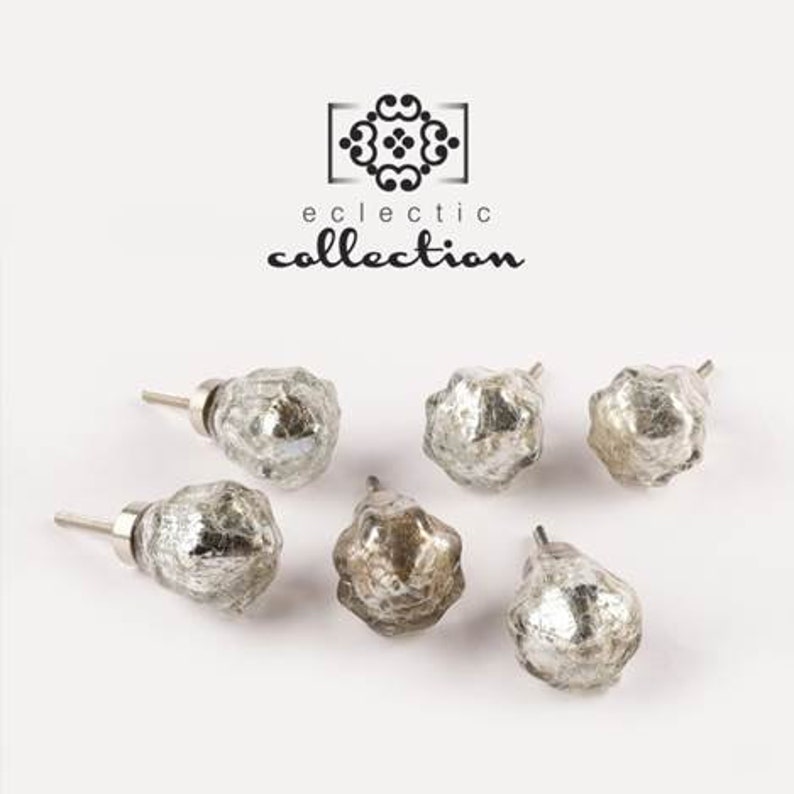 May include: Six silver glass cabinet knobs with a textured, aged finish. The knobs are in various shapes and sizes. The text "eclectic collection" is displayed above the knobs.