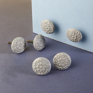 May include: Six gray ceramic drawer knobs with a floral design. The knobs have a silver screw in the back.