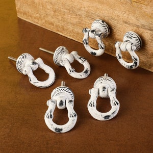 May include: Set of six white metal cabinet knobs with a distressed finish. Each knob features a ring-shaped handle with a decorative design.