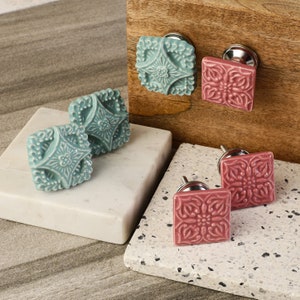 May include: Four ceramic cabinet knobs with intricate floral designs. Two are teal blue and two are pink. Each knob has a silver metal base.