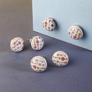 May include: Five white ceramic cabinet knobs with floral designs in shades of pink, red, and green. The knobs have a silver metal base.