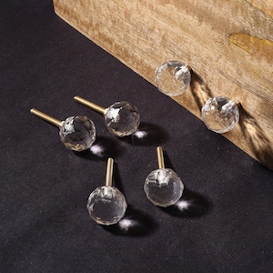 May include: Six clear glass cabinet knobs with gold metal screws. The knobs are faceted and have a round shape.