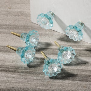 May include: Six blue glass cabinet knobs with a flower design and a clear crystal center. The knobs have a brass screw for attaching to a cabinet door.