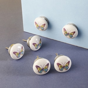 May include: Six white ceramic cabinet knobs with silver accents. Each knob features a colorful butterfly design.
