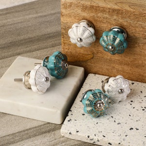 May include: Set of six ceramic cabinet knobs with a decorative floral design. The knobs are in two colors: white with gold accents and teal with gold accents.
