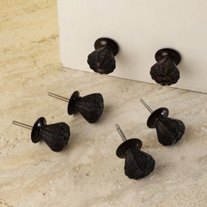May include: Six black metal cabinet knobs with a woven design. The knobs have a round base and a pointed top.