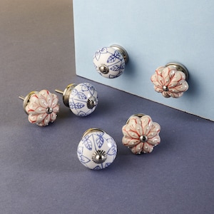 May include: Six ceramic cabinet knobs with floral designs. The knobs are white with blue and red floral patterns. The knobs have a silver metal base.