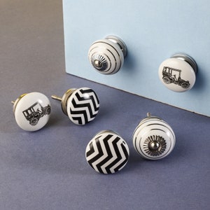 May include: Five ceramic cabinet knobs with a white background and black designs. Two knobs feature a black and white chevron pattern, two knobs feature a vintage car design, and one knob features a simple floral design.