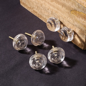 May include: Six clear glass cabinet knobs with a spiral design and gold metal bases.