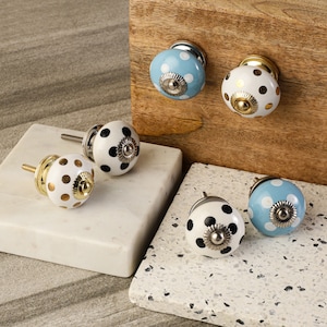 May include: Assortment of four ceramic polka dot knobs in blue and white with gold accents. The knobs have a silver base and are perfect for adding a touch of whimsy to furniture.