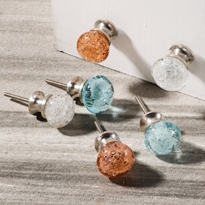 May include: Five glass cabinet knobs with silver metal bases. The knobs are in three colors: light blue, white, and orange. The glass has a textured bubbled appearance.