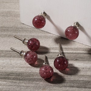 May include: A set of six decorative cabinet knobs. Each knob features a round, bubble-textured, deep-red glass orb with a silver-toned metal base and screw. Two knobs are attached to a white surface, while the others are loose on a gray surface.