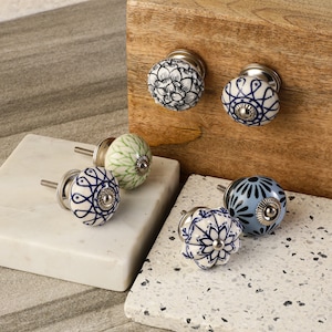 May include: Assortment of six ceramic cabinet knobs with various blue and white floral patterns. The knobs have a silver metal base and are displayed on a wooden surface and a white surface.