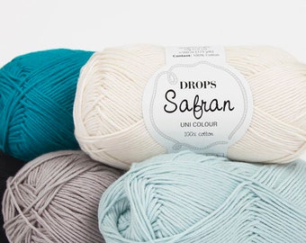 May include: Four balls of yarn in different colors: teal, white, gray, and light blue. The white ball has a label that reads "DROPS Safran UNI COLOUR 100% cotton".