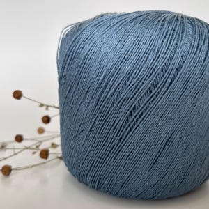 May include: A large ball of blue yarn, likely for knitting or crocheting, is the focal point of this image. The yarn has a textured appearance, with visible strands. Dried flower stems with small brown buds are in the background, adding a touch of natural detail.
