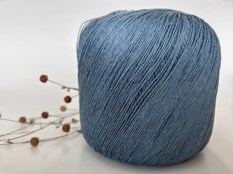 May include: A large ball of blue yarn, likely for knitting or crocheting, is the focal point of this image. The yarn has a textured appearance, with visible strands. Dried flower stems with small brown buds are in the background, adding a touch of natural detail.