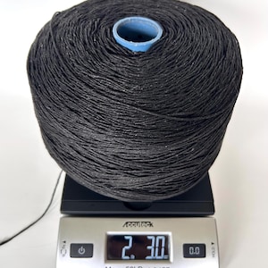 May include: A large spool of black yarn wound around a light blue plastic core, resting on a silver digital scale. The scale display shows a weight of 2 pounds and 3.0 ounces, with a maximum capacity of 50 pounds and a resolution of 0.1 ounces.