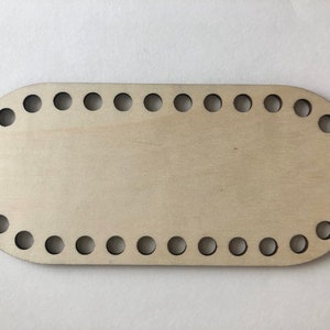 May include: A wooden oval loom with 24 holes around the edge. The loom is made of light brown wood and is perfect for creating small crocheted projects.