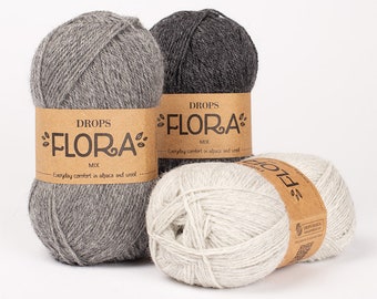 May include: Three balls of Drops Flora Mix yarn in shades of gray and off-white. Each ball has a brown paper label with the text "DROPS FLORA MIX" and "Everyday comfort in alpaca and wool."