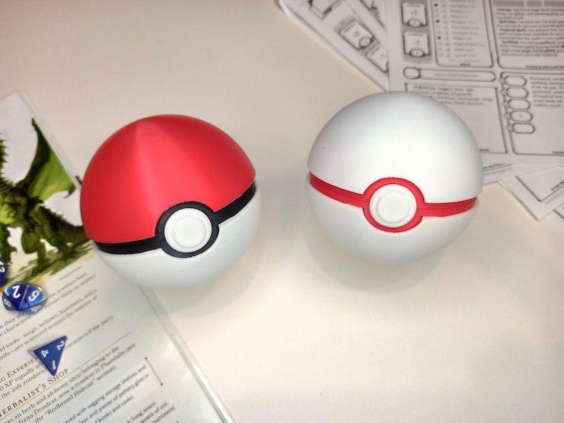 May include: Two Poke Balls, one red and white and one white with a red ring. The Poke Balls are on a white surface.