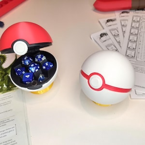 May include: Two Pokeball dice containers, one open with blue dice inside, the other closed. The open container is red and white with a black rim. The closed container is white with a red rim.