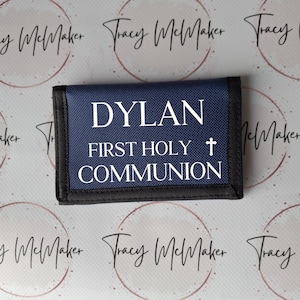 May include: A blue fabric wallet with a black trim. The wallet has white text that reads "DYLAN FIRST HOLY + COMMUNION".