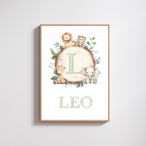 May include: A framed print with a watercolour illustration of a wooden log bearing the letter "L" and the name "LEO" in light green. The log is surrounded by jungle animals: a lion, tiger, giraffe, and elephant. The artwork has a soft, pastel colour palette.