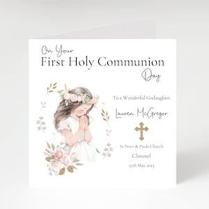 Op de afbeelding: Een witte kaart met een aquarel-illustratie van een meisje in een witte jurk met een bloemenkrans, dat bidt. De kaart zegt "On Your First Holy Communion Day" en "To a Wonderful Goddaughter Lauren McGregor". De kaart bevat ook de naam van de kerk, "St Peter & Pauls Church Clonmel", en de datum "27th May 2023".