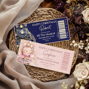 May include: Two decorative tickets featuring train illustrations. One is navy blue with gold detailing, reading "Happy Christmas Robert" and "Elf The Musical". The other is pink with gold accents, reading "Happy Christmas Sophia" and "Beauty and the Beast".