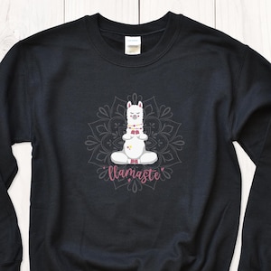 Op de afbeelding: Zwart sweatshirt met een witte lama die mediteert in een mandala-ontwerp. De tekst "llamaste" is onder de lama gedrukt.