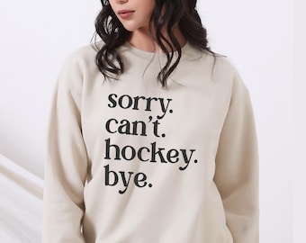 May include: A beige sweatshirt with the text "sorry. can't. hockey. bye." printed in black.