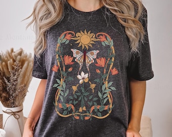 May include: A dark heather grey t-shirt with a floral design featuring a butterfly, sun, and leaves. The design is in shades of orange, yellow, green, and brown.