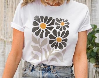 May include: White t-shirt with a graphic of three stylized black and gray flowers with yellow centers.