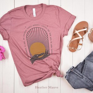 May include: A heather mauve t-shirt with a graphic design of a hand reaching for a sun with the text "The universe is full of magical things patiently waiting for our wits to grow sharper".