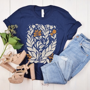 May include: A navy blue t-shirt with a white and orange floral design. The shirt is paired with light blue jeans and nude platform heels.
