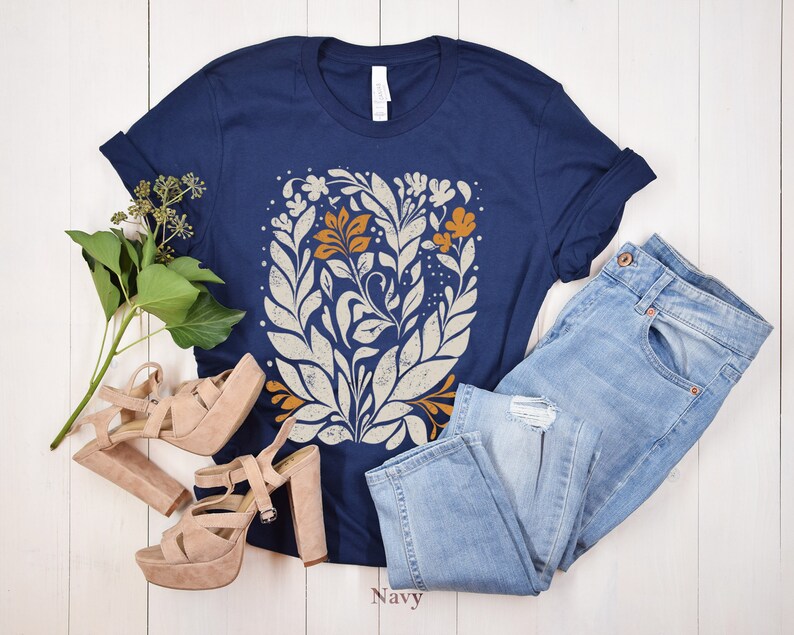 May include: A navy blue t-shirt with a white and orange floral design. The shirt is paired with light blue jeans and nude platform heels.