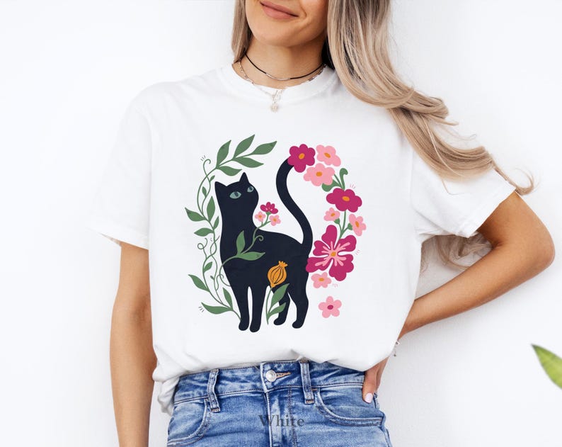 Pu&ograve; includere: Una t-shirt bianca con un'illustrazione grafica di un gatto nero circondato da viti verdi e vari fiori rosa e rossi. Il gatto &egrave; raffigurato di profilo, rivolto verso l'alto, con la coda elegantemente curva tra gli elementi floreali.