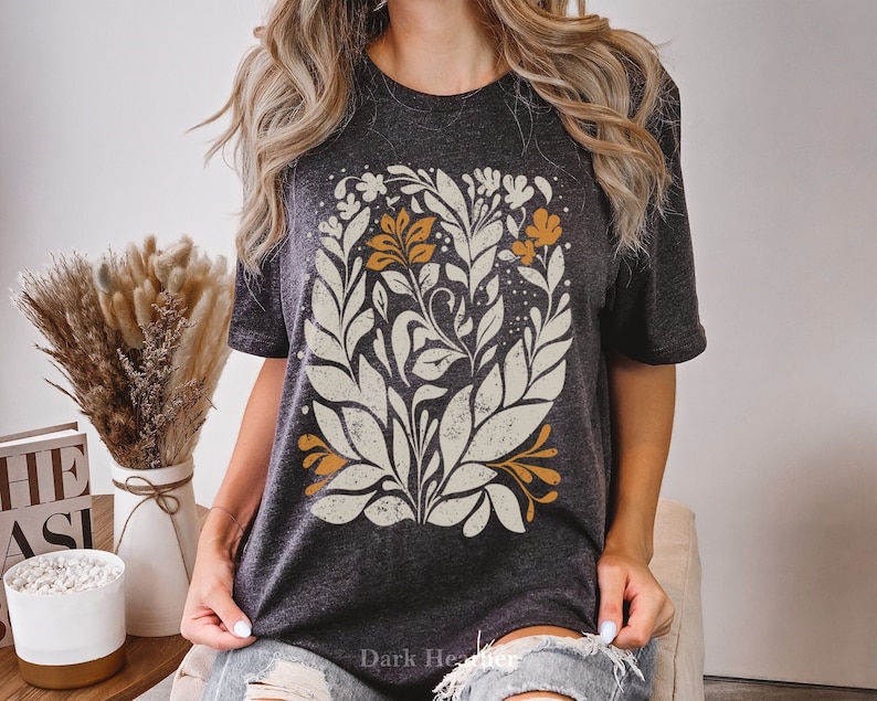 May include: A dark heather grey t-shirt with a white and orange floral design. The design features leaves and flowers in a vintage style.