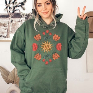 May include: A green hooded sweatshirt with a graphic print of a smiling sun surrounded by red and orange flowers.