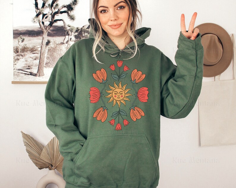 May include: A green hooded sweatshirt with a graphic print of a smiling sun surrounded by red and orange flowers.