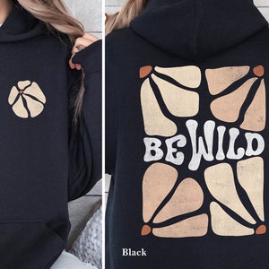 Op de afbeelding: Zwarte hoodie met een grafische print van een geometrisch ontwerp en de tekst "BE WILD" in wit.