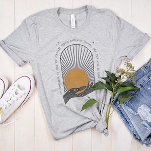 May include: A gray t-shirt with a graphic design of a hand holding a sun with the text "The universe is full of magical things patiently waiting for our wits to grow".
