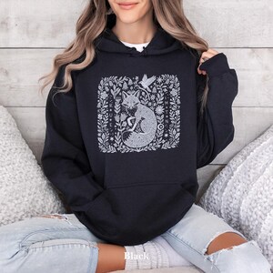 May include: Black hooded sweatshirt featuring a white illustration of a fox within a floral design. The word "Black" is printed at the bottom. The sweatshirt has a hood with a drawstring and long sleeves. The design is on the front.