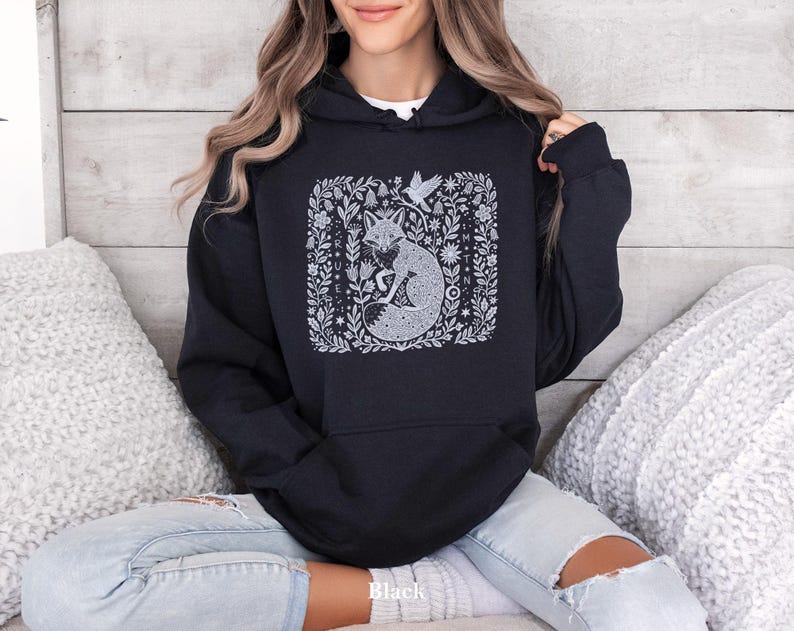 May include: Black hooded sweatshirt featuring a white illustration of a fox within a floral design. The word "Black" is printed at the bottom. The sweatshirt has a hood with a drawstring and long sleeves. The design is on the front.
