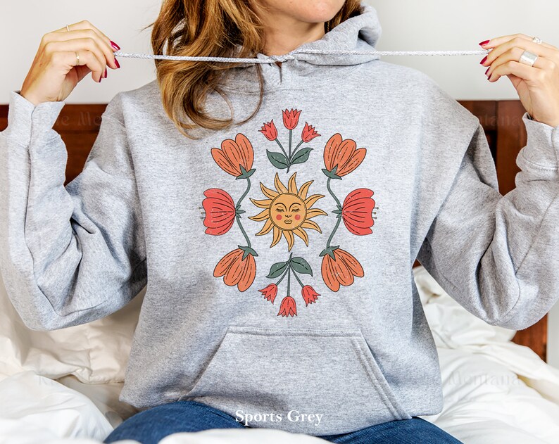 May include: A gray hooded sweatshirt with a graphic print of a sun with a face and flowers in shades of orange, red, and green. The text "Sports Grey" is printed on the bottom of the sweatshirt.
