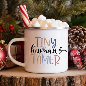 May include: White enamel mug with a red and white candy cane, marshmallows, and the text "TINY human TAMER" in colourful lettering.
