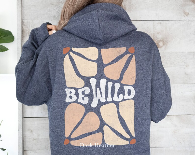 Op de afbeelding: Donkergrijs hoodie met een witte afbeelding van abstracte vormen en de tekst "BE WILD" in een retro-lettertype.