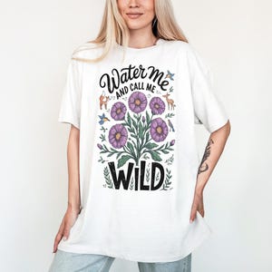 May include: White t-shirt with a floral design and the text "Water me and call me wild".