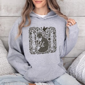 May include: A grey hoodie featuring a dark green illustration of a fox within a floral frame, with a bird. The hoodie has a drawstring hood and a front pocket. The text "Sports Grey" is visible at the bottom.